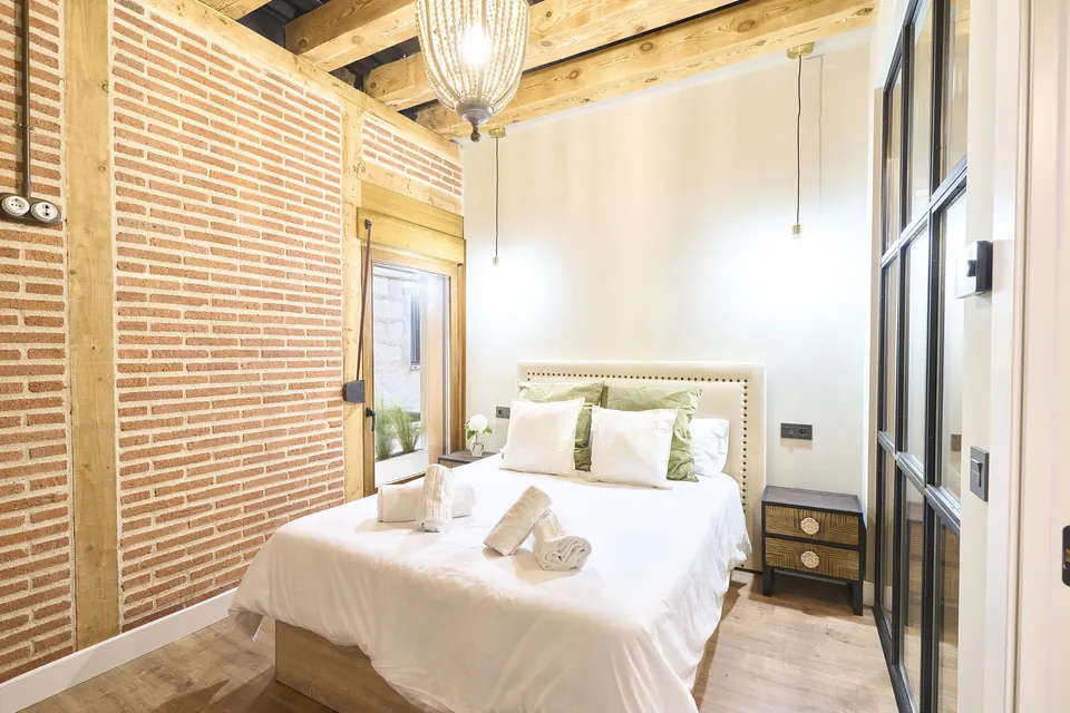 Dormitorio con cabecero tapizado, cojines verdes y ventana a un patio